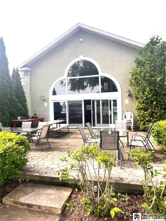 rear view of house featuring outdoor dining area, a patio, and stucco siding