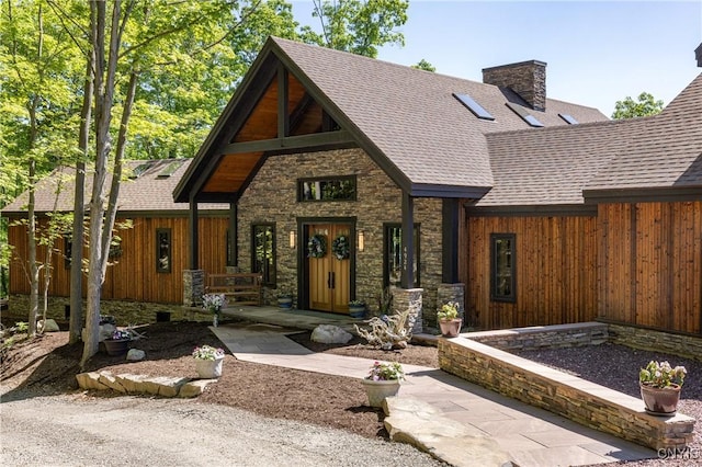 view of front of house featuring stone siding, a chimney, a porch, and roof with shingles