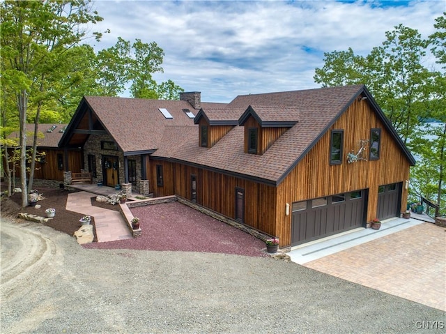 chalet / cabin featuring a garage, covered porch, a shingled roof, stone siding, and decorative driveway