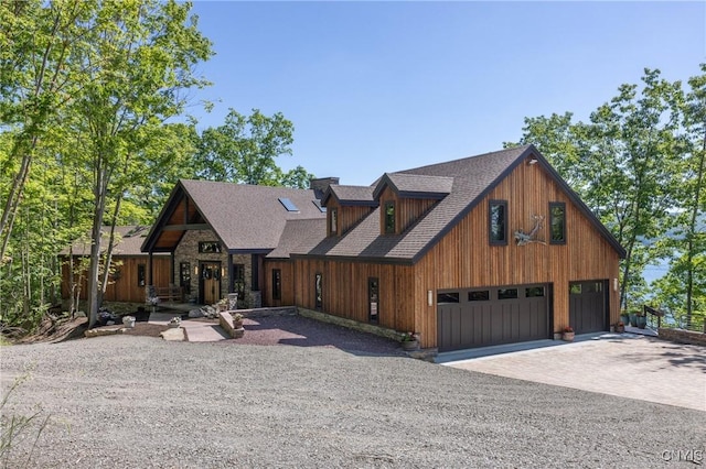 chalet / cabin featuring an attached garage, driveway, a shingled roof, and stone siding