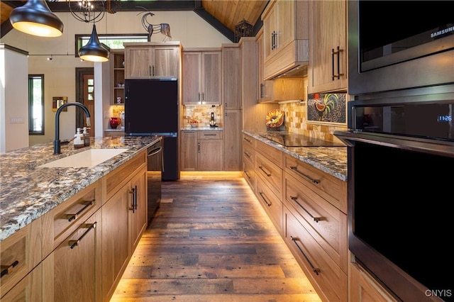 kitchen with dark wood-type flooring, a sink, appliances with stainless steel finishes, tasteful backsplash, and dark stone countertops