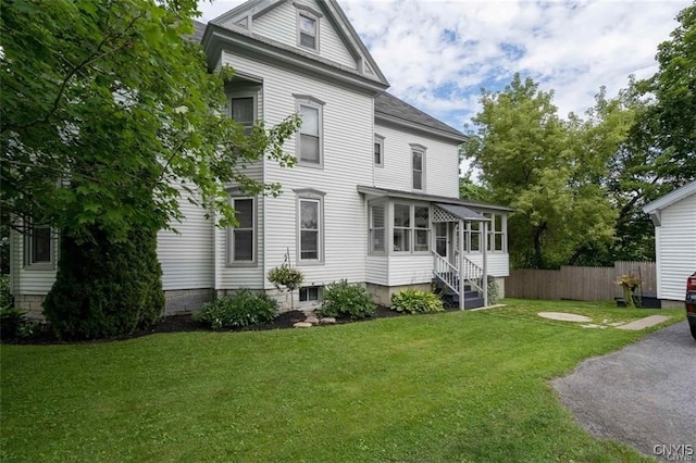 view of front of house with a front yard, a sunroom, and fence