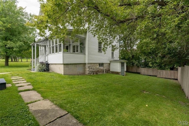 view of home's exterior with an outdoor structure, fence, a sunroom, a yard, and a storage unit