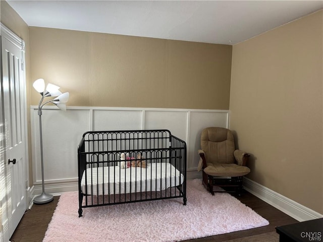 bedroom featuring baseboards, a nursery area, wood finished floors, and a decorative wall