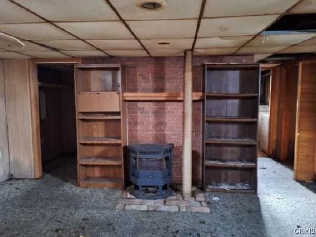 unfurnished living room featuring a wood stove, wood walls, and a paneled ceiling