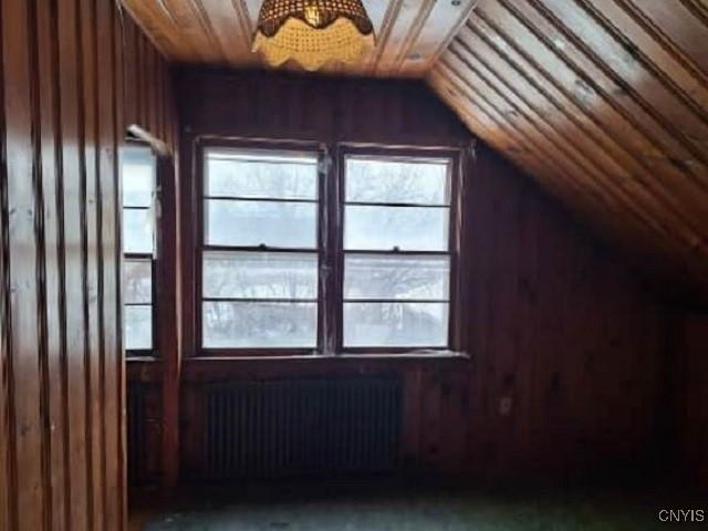 bonus room featuring radiator, wooden walls, vaulted ceiling, and a wealth of natural light