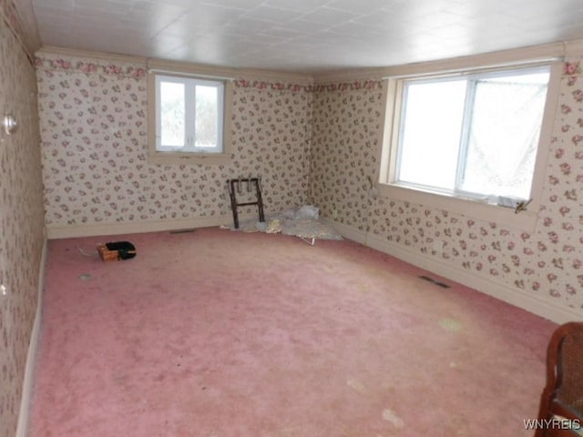 unfurnished room featuring a wealth of natural light, carpet, visible vents, and wallpapered walls