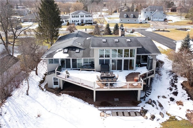 snow covered property with a residential view, a sunroom, and a deck