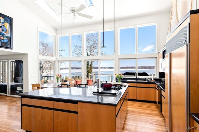 kitchen with ceiling fan, a towering ceiling, appliances with stainless steel finishes, a center island, and light wood finished floors