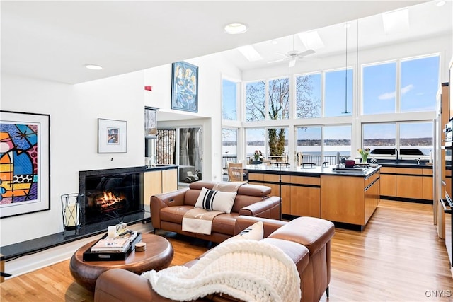 living room featuring a towering ceiling, light wood finished floors, a premium fireplace, and a wealth of natural light