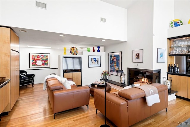 living area featuring light wood-type flooring, a high ceiling, and visible vents