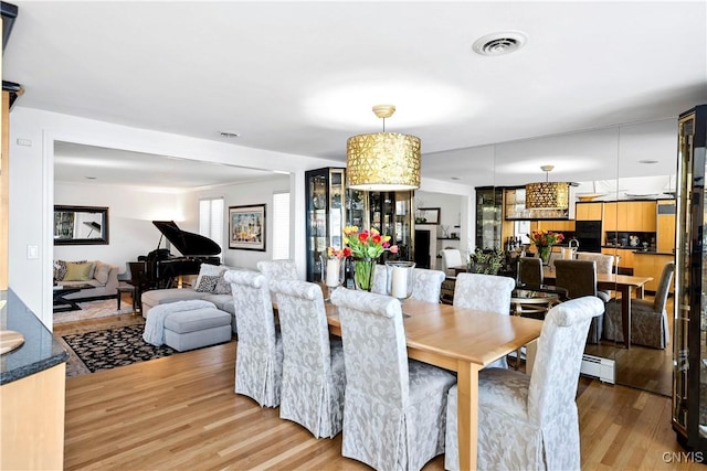 dining room with a baseboard heating unit, visible vents, and light wood finished floors