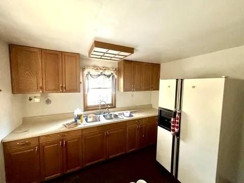 kitchen featuring brown cabinetry, white refrigerator with ice dispenser, light countertops, and a sink