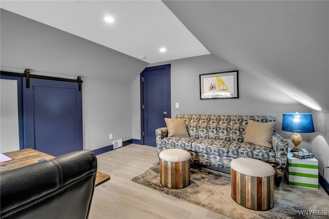 living area with a barn door, visible vents, baseboards, vaulted ceiling, and light wood-type flooring