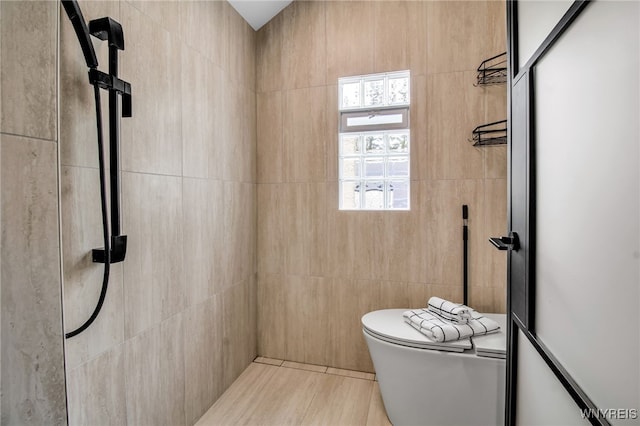 full bathroom featuring toilet, a tile shower, and tile walls