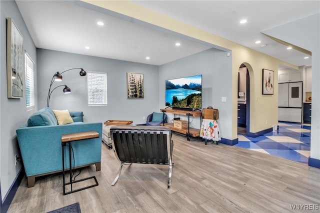 living room with arched walkways, light wood-type flooring, baseboards, and recessed lighting