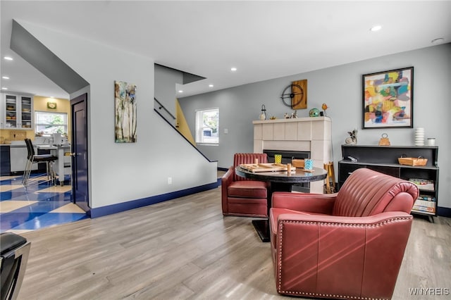 living room featuring baseboards, a tiled fireplace, light wood-style flooring, and a healthy amount of sunlight