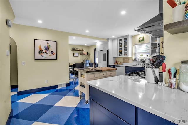 kitchen with dishwashing machine, wall chimney exhaust hood, dark floors, a center island, and freestanding refrigerator