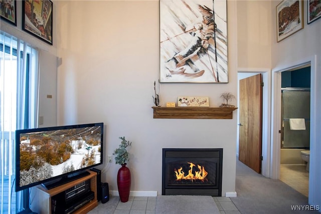 living area featuring tile patterned flooring, a high ceiling, baseboards, and a glass covered fireplace