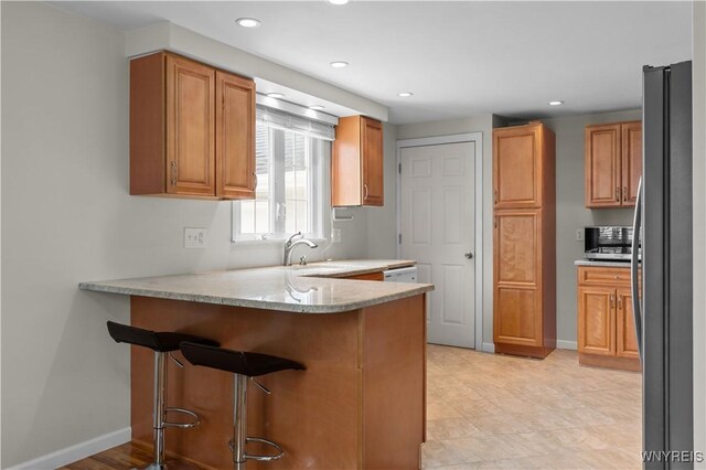 kitchen featuring baseboards, a breakfast bar, freestanding refrigerator, a peninsula, and a sink