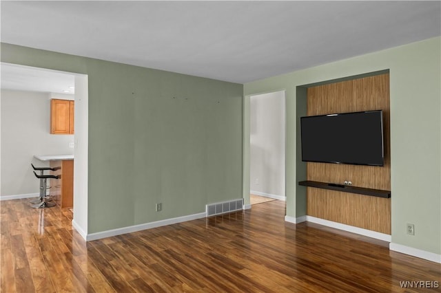 unfurnished living room featuring visible vents, baseboards, and wood finished floors