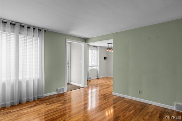 empty room with wood finished floors, visible vents, and baseboards