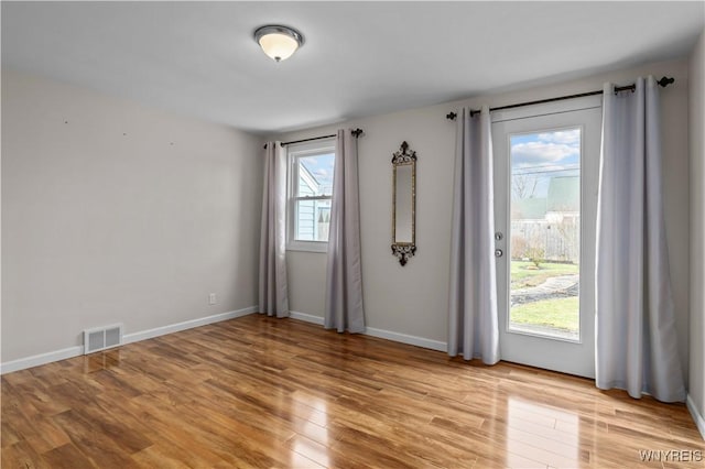 empty room with light wood-style floors, visible vents, and baseboards