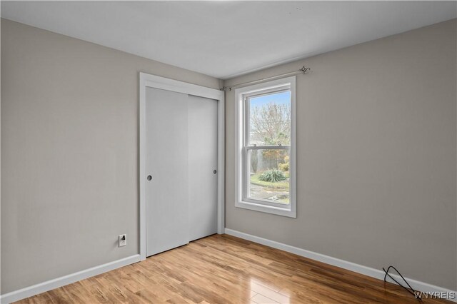 unfurnished bedroom featuring light wood finished floors, baseboards, and a closet