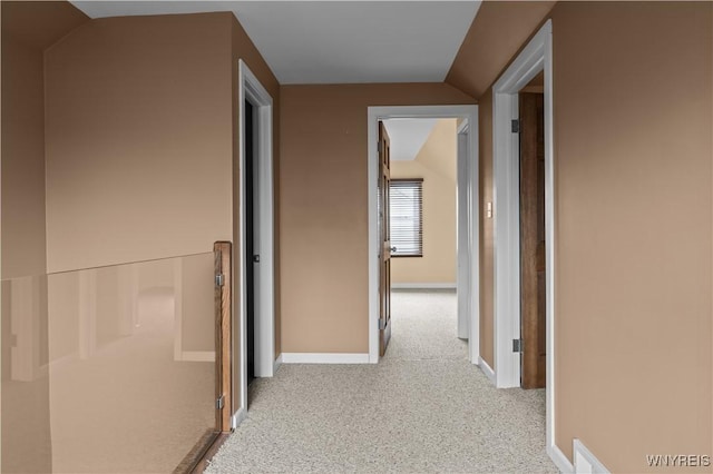 corridor with lofted ceiling, carpet flooring, and baseboards