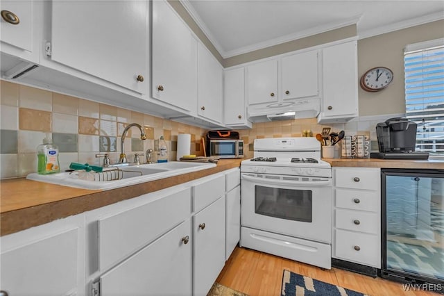 kitchen featuring white gas range oven, wine cooler, crown molding, under cabinet range hood, and white cabinetry