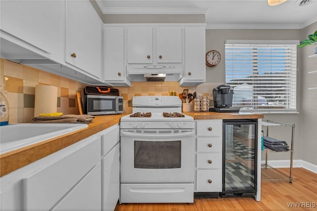 kitchen featuring under cabinet range hood, beverage cooler, stainless steel microwave, gas range gas stove, and crown molding