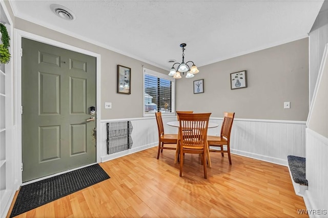 dining room with visible vents, wainscoting, an inviting chandelier, crown molding, and light wood-type flooring