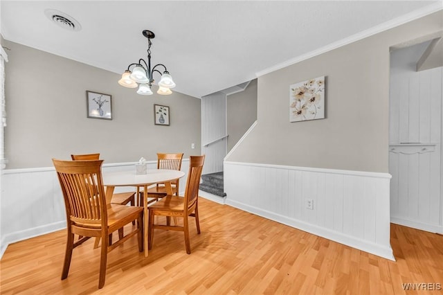 dining area featuring wainscoting, visible vents, light wood finished floors, and stairs