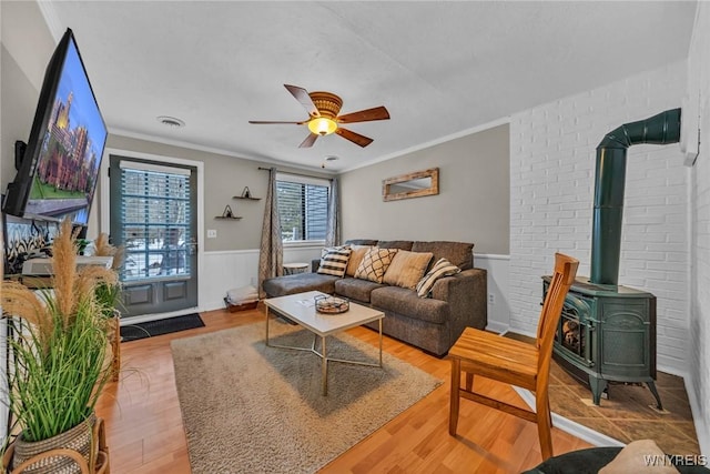 living area with a wood stove, a wainscoted wall, ceiling fan, and ornamental molding