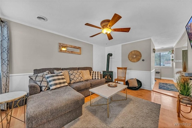 living area with a wainscoted wall, a wood stove, wood finished floors, and visible vents