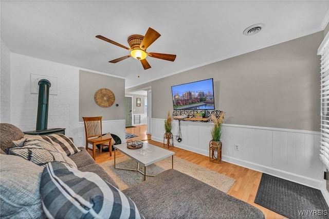 living room with visible vents, a ceiling fan, a wainscoted wall, wood finished floors, and a wood stove