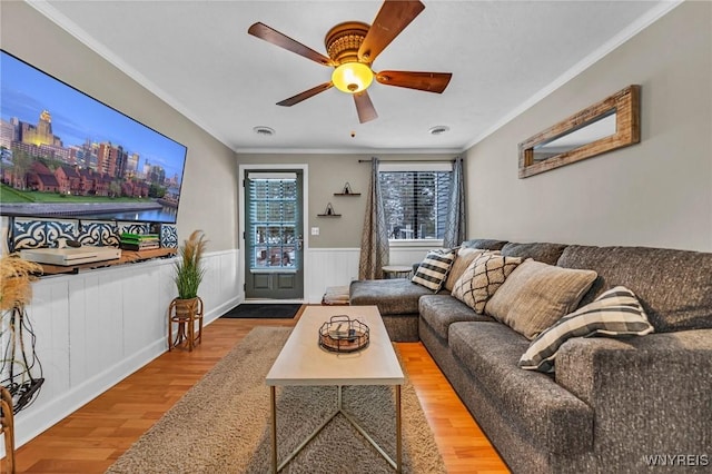 living area featuring ornamental molding, a wainscoted wall, visible vents, and wood finished floors