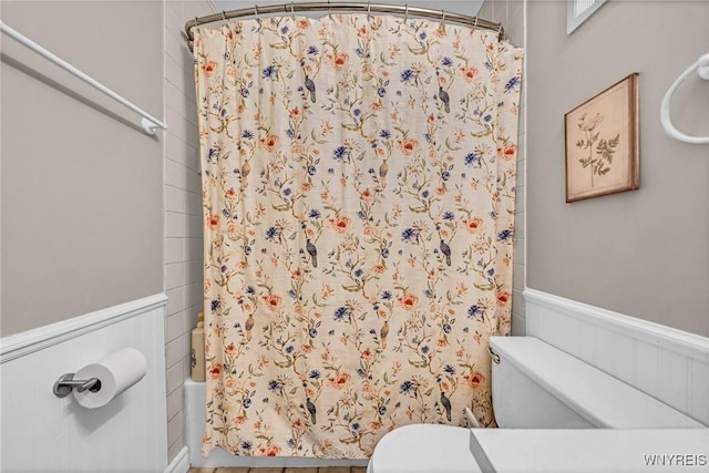 bathroom with a wainscoted wall, shower / bath combo, and toilet