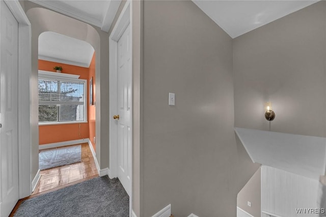 hallway featuring arched walkways, carpet, and baseboards