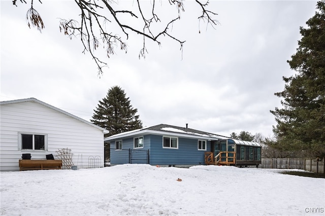 snow covered rear of property featuring fence and a sunroom