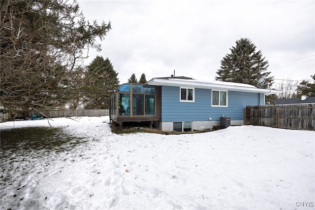 snow covered property with fence, a sunroom, and central air condition unit