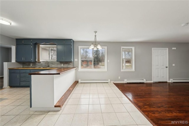 kitchen with a peninsula, baseboard heating, a sink, and light tile patterned flooring