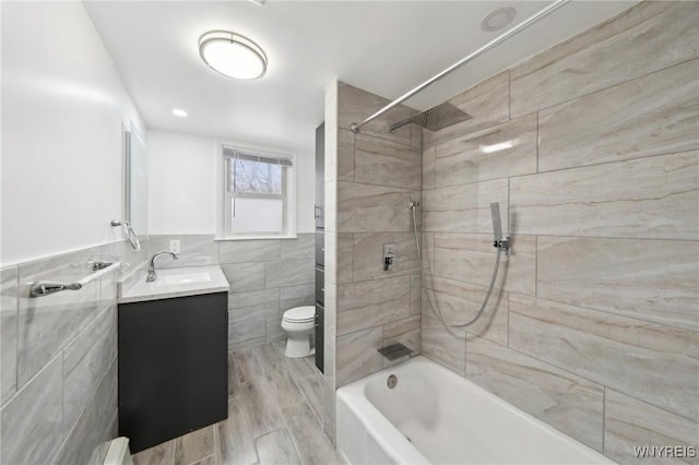 full bathroom with toilet, wood tiled floor, vanity, shower / washtub combination, and tile walls