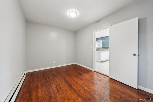 unfurnished room featuring baseboard heating, hardwood / wood-style flooring, and baseboards