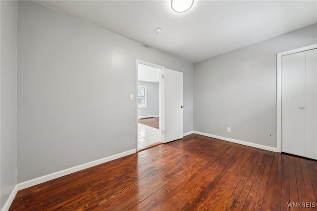 unfurnished bedroom featuring a closet, a baseboard radiator, wood-type flooring, and baseboards