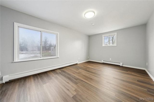 empty room featuring baseboard heating, wood finished floors, and baseboards