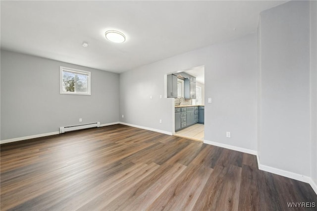 unfurnished bedroom featuring a baseboard heating unit, a sink, ensuite bath, wood finished floors, and baseboards