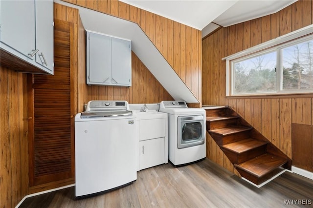 washroom with wood walls, light wood-type flooring, washing machine and clothes dryer, and cabinet space