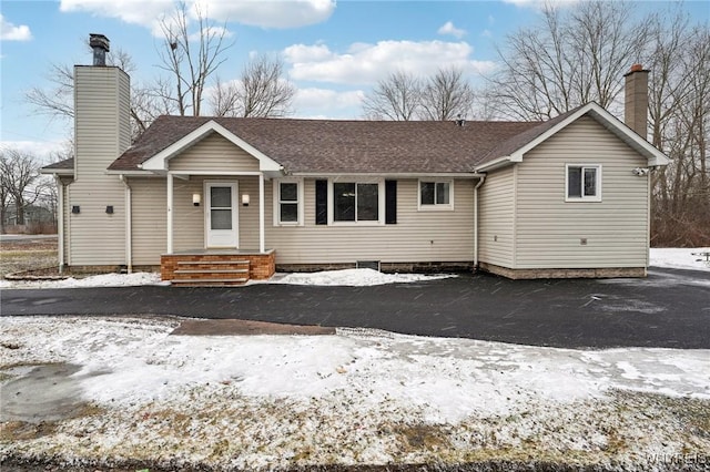 single story home with driveway, a shingled roof, and a chimney