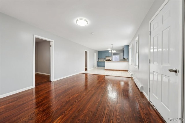 unfurnished living room featuring hardwood / wood-style flooring, a baseboard radiator, baseboards, and a notable chandelier